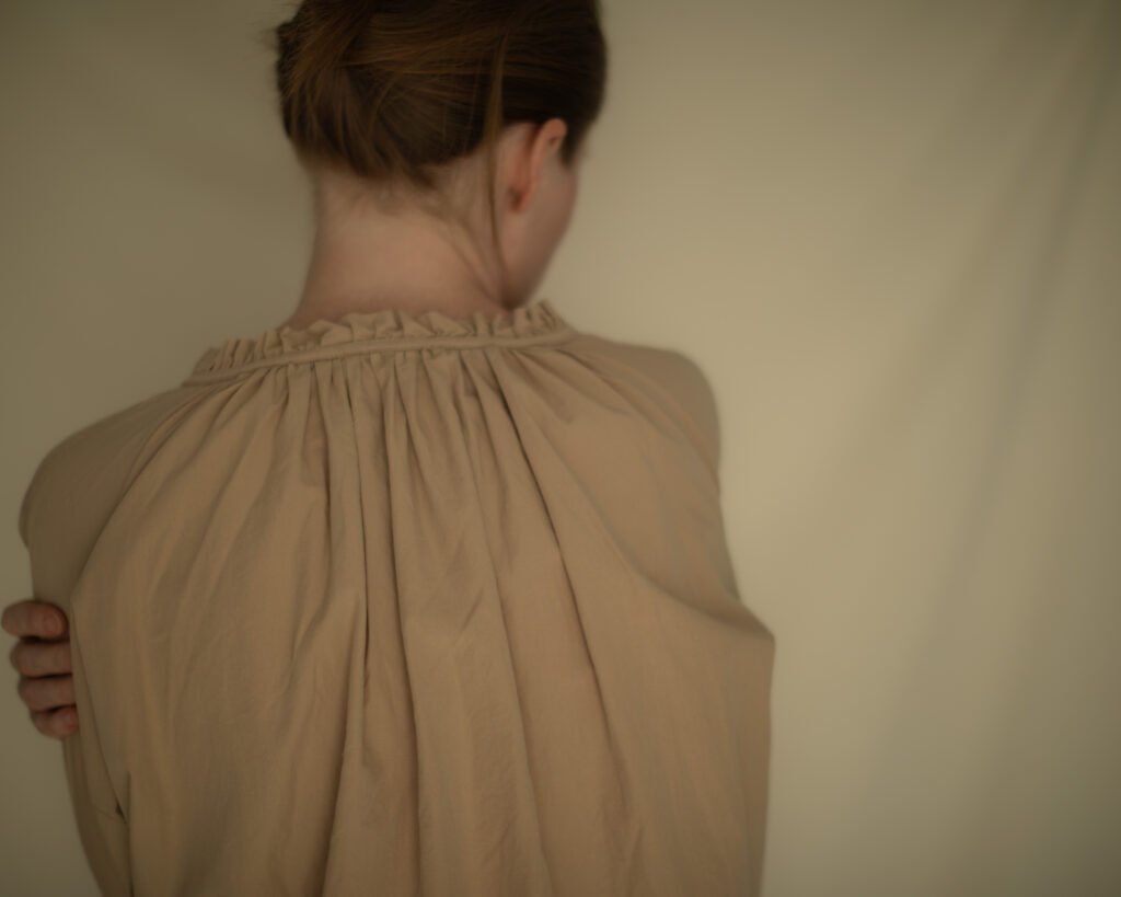 Woman embracing herself in a soft beige garment, exploring comfort and quiet presence