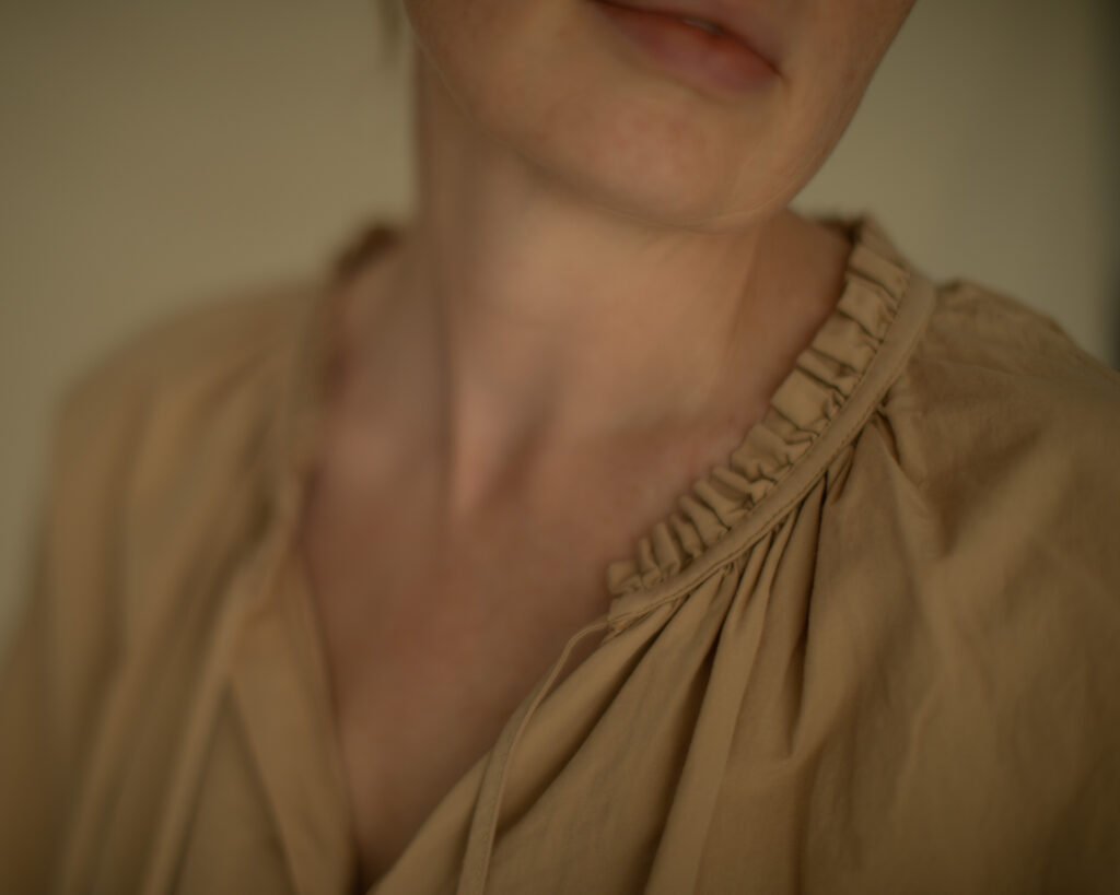 Soft beige garment framing the neck and collarbone in quiet natural light