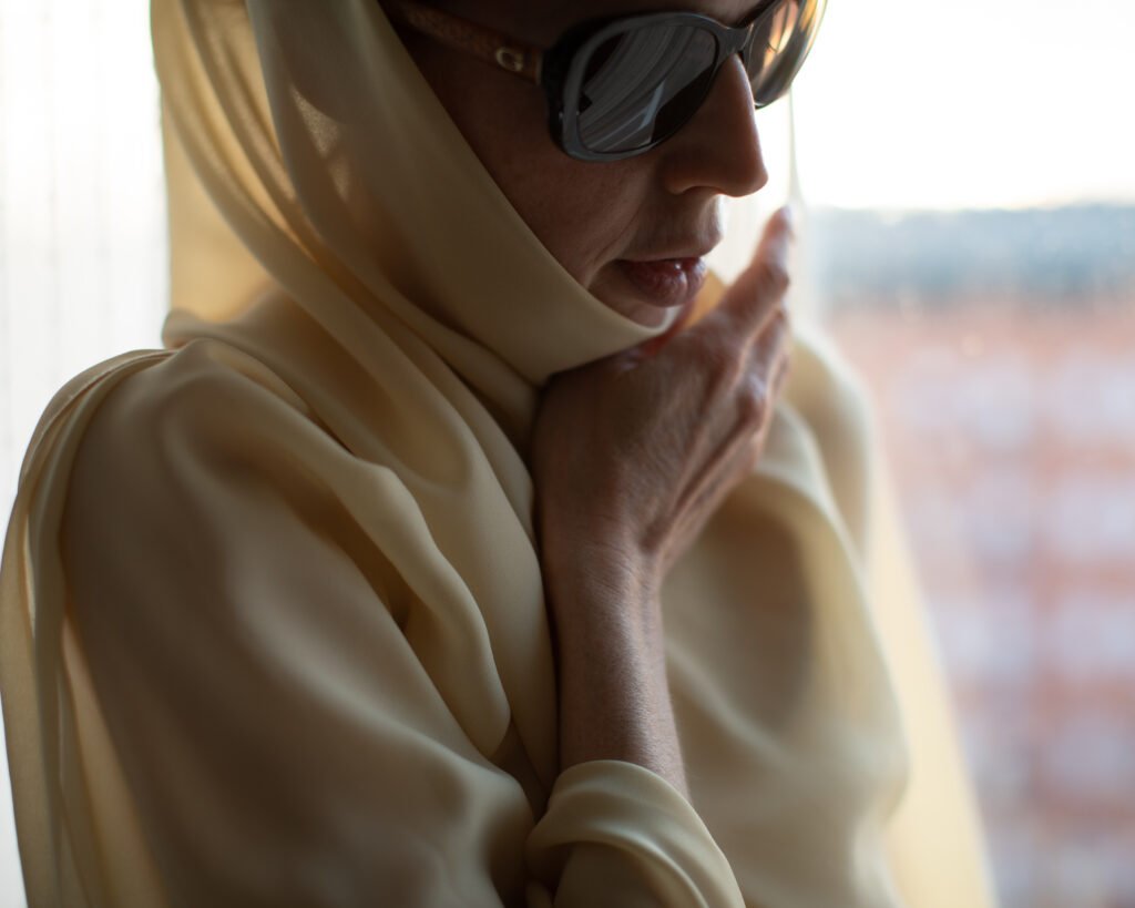Discreet luxury portrait with oversized sunglasses and cream scarf in soft warm light