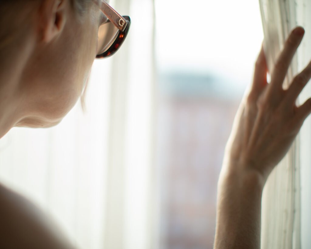 Woman touching window in soft light wearing luxury eyewear