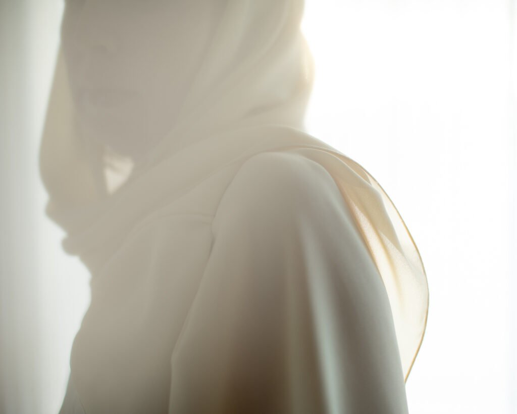 Soft cinematic portrait of a woman in a cream scarf with luxury eyewear in warm window light